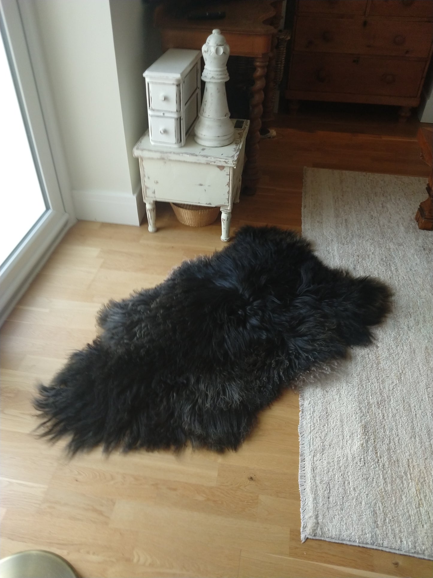 Curly Black Lambskin Rug on the floor showing layering with another rug