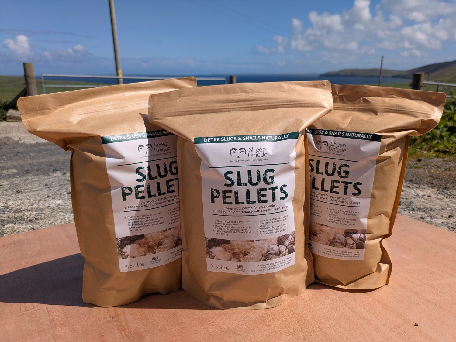 Three bags of slug pellets on a wooden surface with a scenic background.